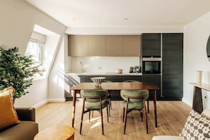 A modern kitchen with a dining area, wooden flooring, and a large window. - Deluxe 2-Bed Belgravia | Sloane Square (London)