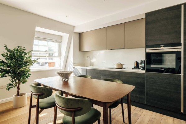 Een moderne keuken met een eettafel en stoelen, een potplant en een raam met gordijnen.