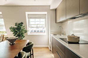 A modern kitchen with a dining area, a window with blinds, and a potted plant. - Deluxe 2-Bed Belgravia | Sloane Square (London)