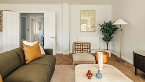 En stue med sofa, lænestol, gulvlampe og en potteplante.