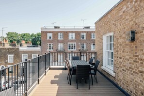 Ein Balkon mit Tisch und Stühlen, eine Backsteinmauer und ein Nachbargebäude mit mehreren Fenstern.
