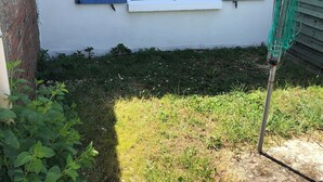 Ein Fenster mit blauen Fensterläden, eine Ziegelwand und eine Rasenfläche mit einem Gartenschlauch.