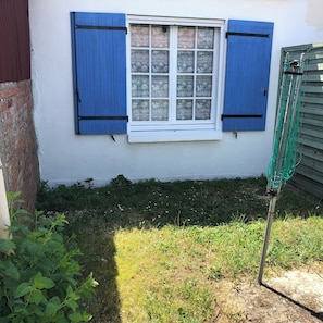 Ein Fenster mit blauen Fensterläden, eine Ziegelwand und eine Rasenfläche mit einem Gartenschlauch.