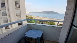 A balcony with a view of the beach and mountains, a small table, and a chair. - SHB Pé na Areia Piscina Vista Incrível (Santos)
