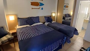 A hotel room with two beds, striped bedding, a nightstand with a lamp, a chair, and a mirror on the wall. - SHB Pé na Areia Piscina Vista Incrível (Santos)