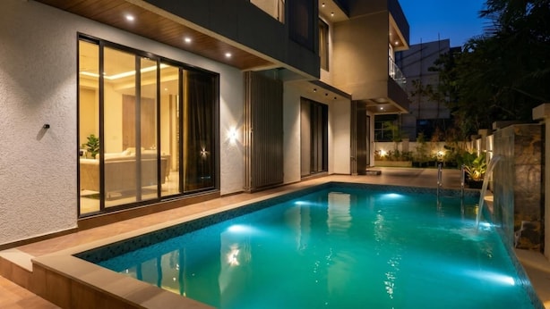 Un espace moderne aménagé au bord de la piscine, comprenant une piscine, des portes vitrées et un éclairage extérieur soigné.