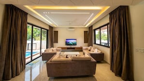 Un salon moderne doté d’un grand téléviseur à écran plat, d’un ensemble de canapés et offrant une vue sur une piscine.