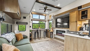 Interior compacto de una caravana con kitchenette, zona de comedor y espacio de estar con sofá y sillones.