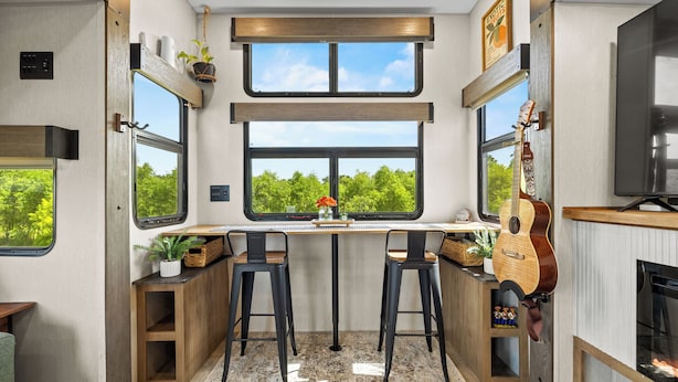 Cocina compacta con una isla central, taburetes de bar y un amplio ventanal con vista a zonas verdes.