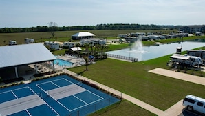 Un espacio recreativo con piscina, canchas de tenis, vehículos recreativos y una fuente.