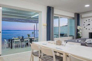 A room with a dining table, chairs, a sofa, a clock, and a view of the sea. - Beachfront Villa with Spa Pool (Podstrana)