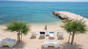 Ein Strand mit Liegestühlen, einem kleinen Tisch und einem Baum.