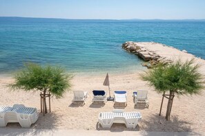 Ein Strand mit Liegestühlen, einem kleinen Tisch und einem Baum.