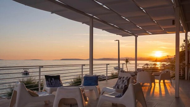 Eine Terrasse mit weißen Plastikstühlen und Blick auf den Sonnenuntergang über dem Wasser.