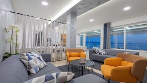 Ein modernes Wohnzimmer mit einer Couch, Sesseln, einem Couchtisch und Blick auf den Ozean.