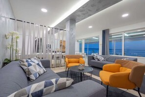 Ein modernes Wohnzimmer mit einer Couch, Sesseln, einem Couchtisch und Blick auf den Ozean.