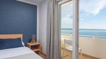 A hotel room with a bed, a nightstand, a lamp, and a view of the sea through a sliding glass door.