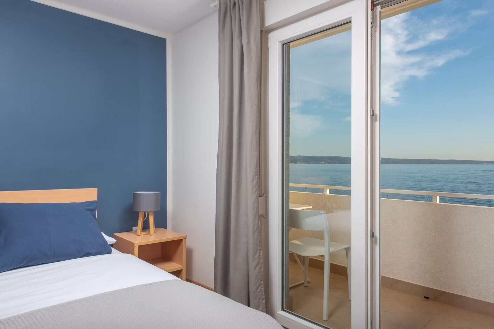 Een hotelkamer met een bed, nachtkastje, lamp en een schuifdeur naar een balkon met uitzicht op zee.