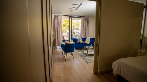 Une pièce comprenant un lit, un canapé bleu, une table à manger avec des chaises, et donnant sur l’extérieur grâce à une porte coulissante.
