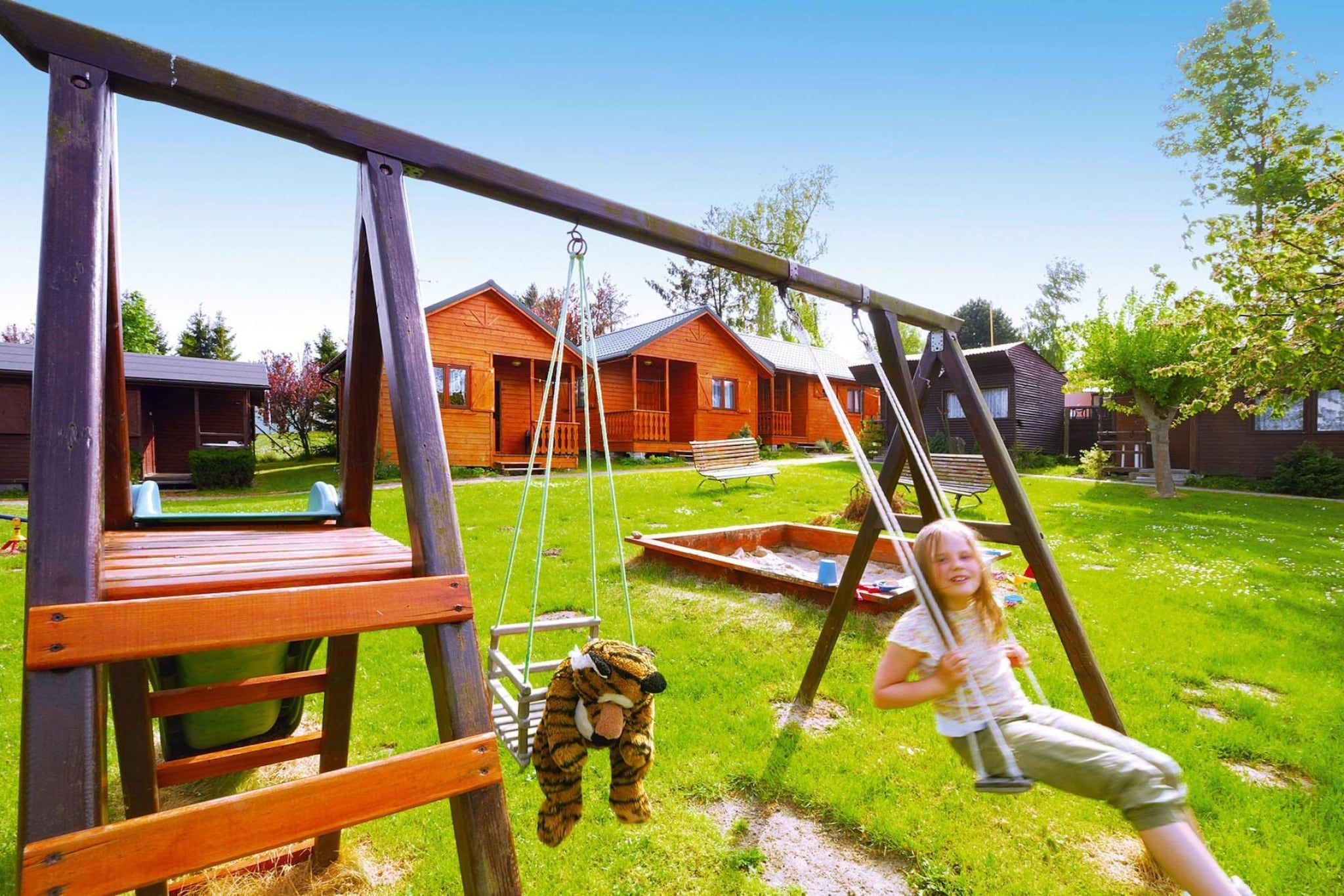 A wooden swing set in a grassy yard with a house in the background.