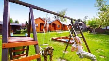 A wooden swing set in a grassy yard with a house in the background.