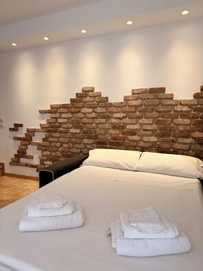 A bedroom with a brick-patterned headboard, a bed with white linens, and a bedside table. - "Corte Magnolia Lazise" Vacation Home, Between the Thermal Springs and Lake Garda (Colà)