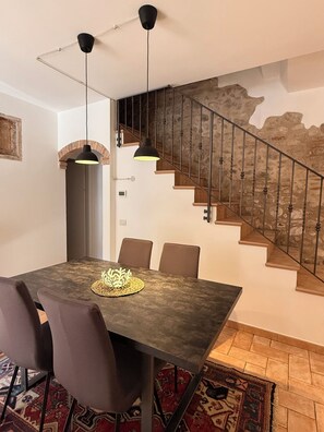 A dining area with a table, chairs, and a staircase with a stone wall. - "Corte Magnolia Lazise" Vacation Home, Between the Thermal Springs and Lake Garda (Colà)