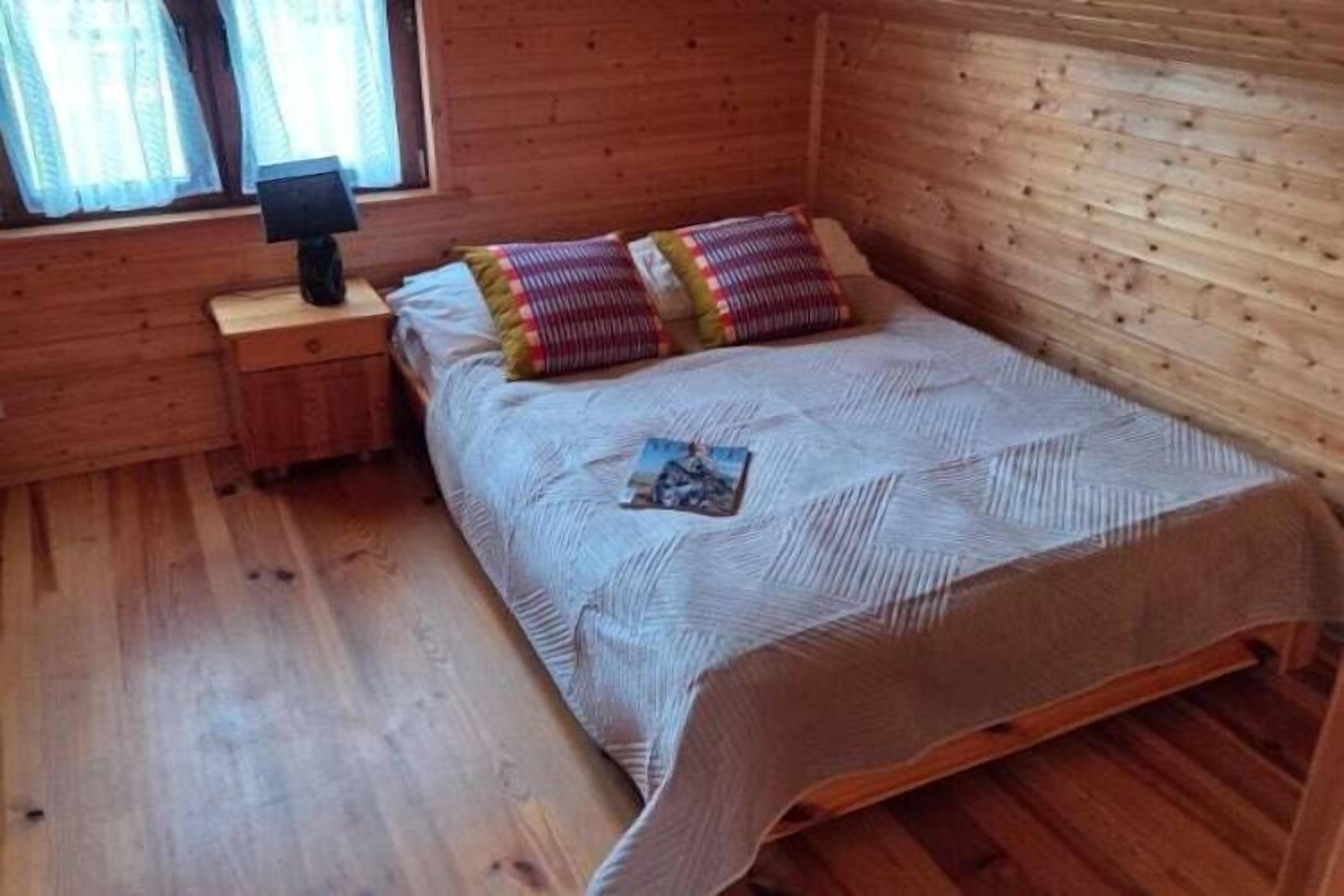 Um quarto de madeira com uma cama, uma mesa de cabeceira e uma janela.