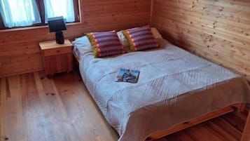 Um quarto de madeira com uma cama, uma mesa de cabeceira e uma janela.