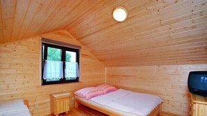A single bed with a pink blanket, a small wooden nightstand, a television, and a window with curtains. - Holiday home with a terrace, close to the sea (Sianozety)