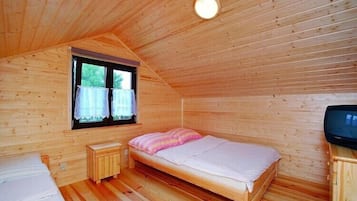 Uma cama de solteiro com um cobertor rosa, uma pequena mesa de cabeceira de madeira, uma televisão e uma janela com cortinas.