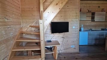 Interior em madeira com escada, televisão na parede e área de cozinha.