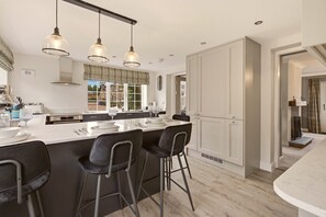 A modern kitchen with a central island, bar stools, pendant lighting, and a view to the outside. - The Cottage - Powburn - North East Escapes (Powburn)