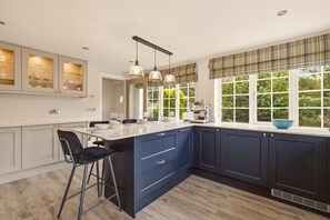 A modern kitchen with a central island, bar stools, pendant lighting, and a view through large windows.