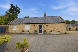 A stone building with a dark roof, a central door, and two windows on either side.