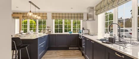 A modern kitchen with dark cabinetry, a central island, pendant lighting, and large windows.