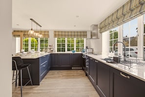 A modern kitchen with dark cabinetry, a central island, pendant lighting, and large windows. - The Cottage - Powburn - North East Escapes (Powburn)