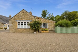 A stone cottage with a gravel driveway, a green fence, and a small garden area. - The Cottage - Powburn - North East Escapes (Powburn)