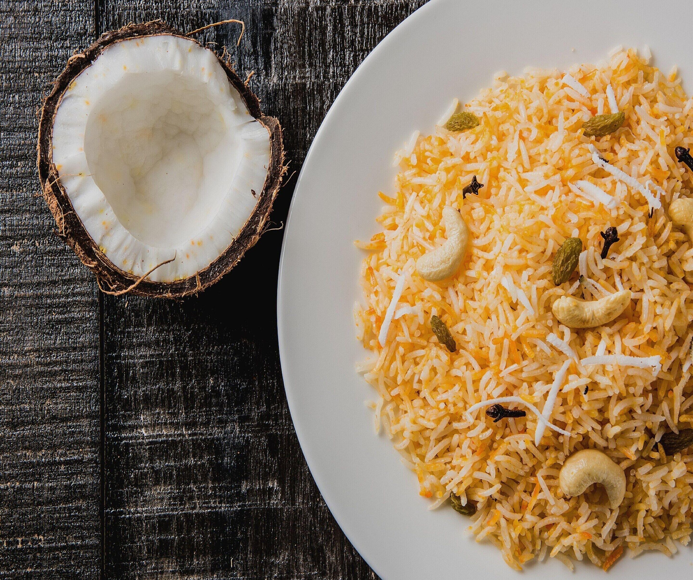 A plate of rice with cashew nuts and raisins on a wooden surface.