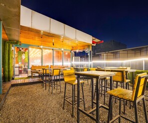 An outdoor seating area with tables and chairs, a wooden ceiling, and a view of the building's interior. - Townhouse Oak Silver City Chowk (Dehradun)