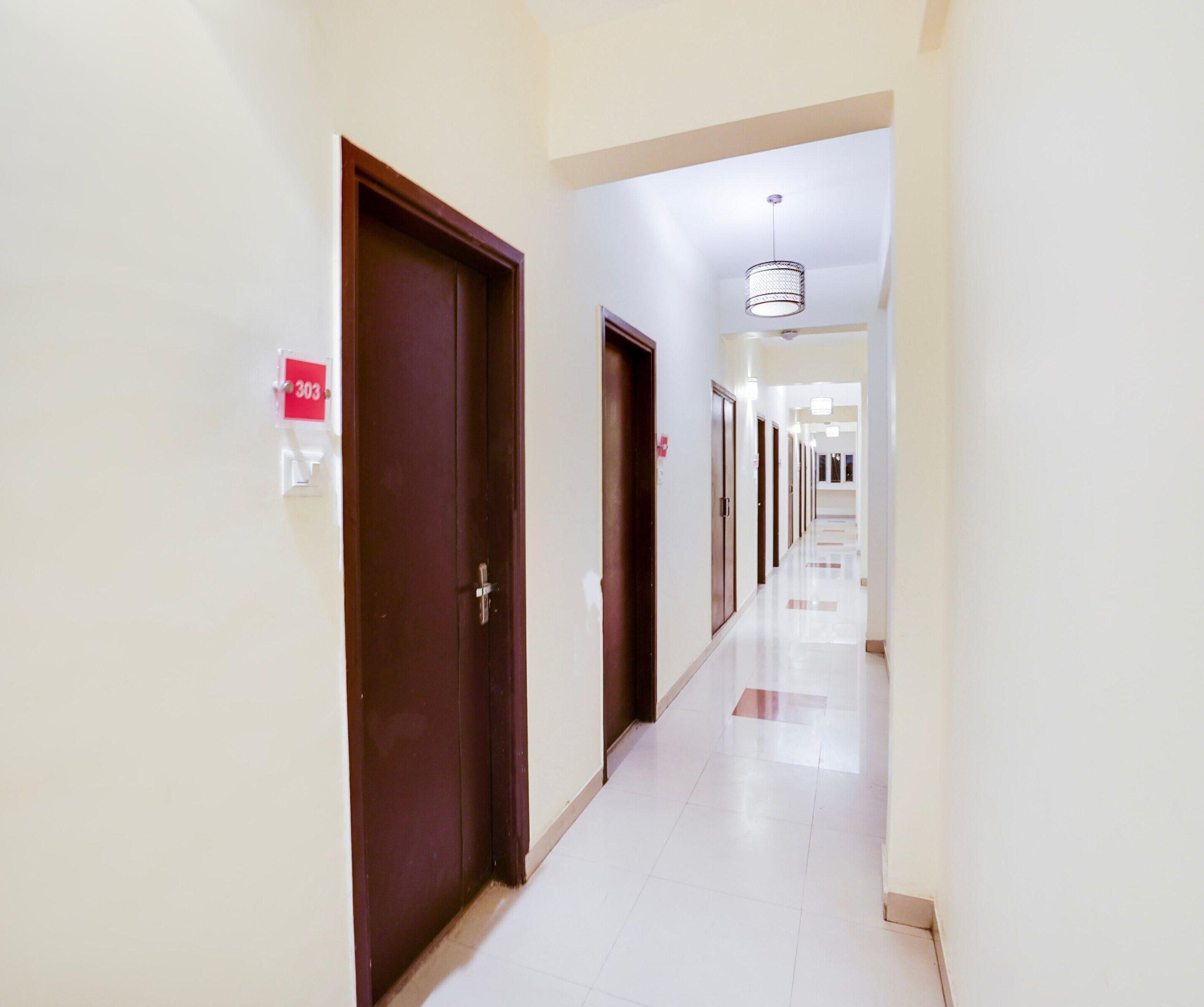 A hotel corridor with doors, a sign indicating room number 303, and a modern light fixture.