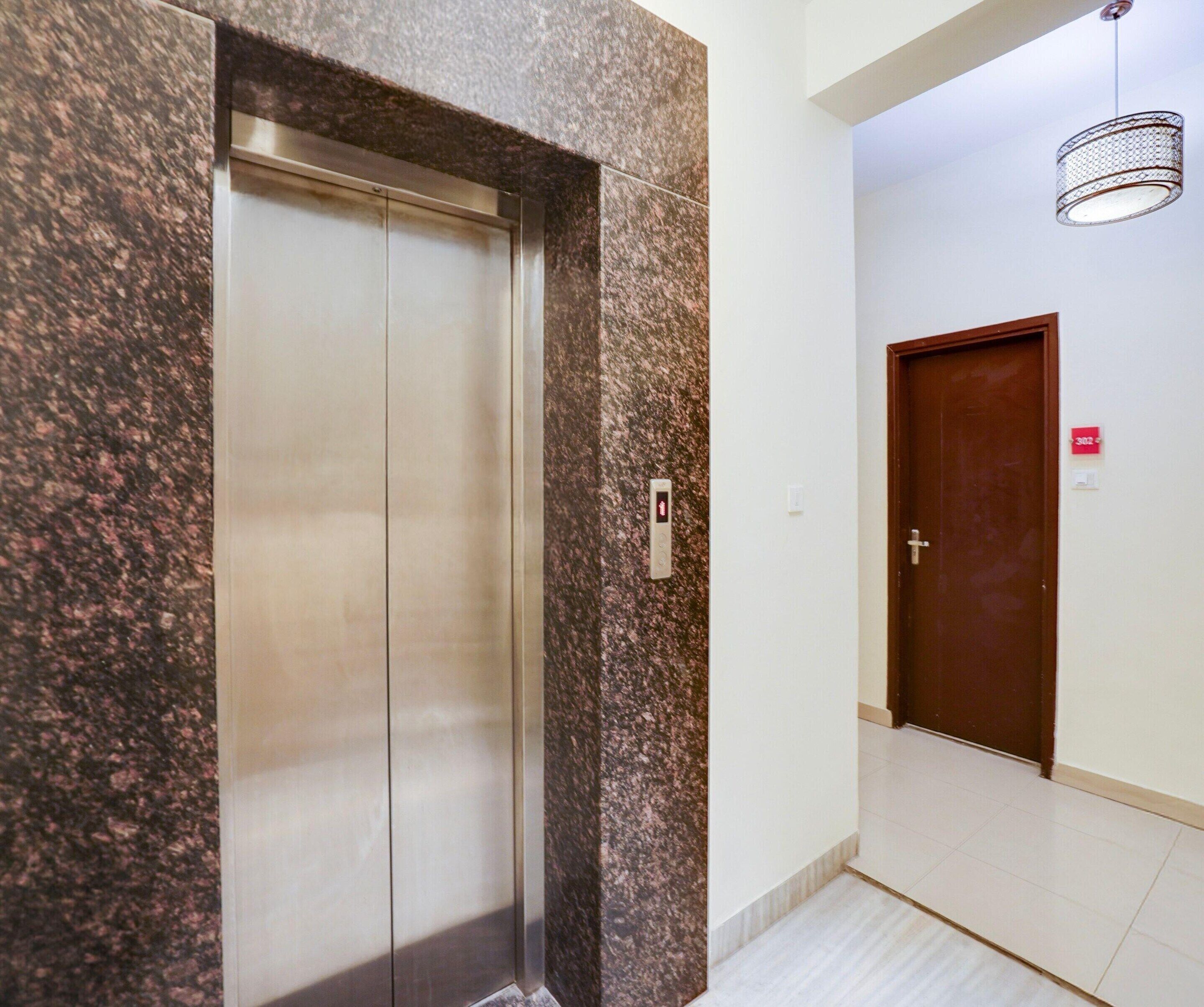 An elevator with a metallic finish and a wall with a speckled pattern.