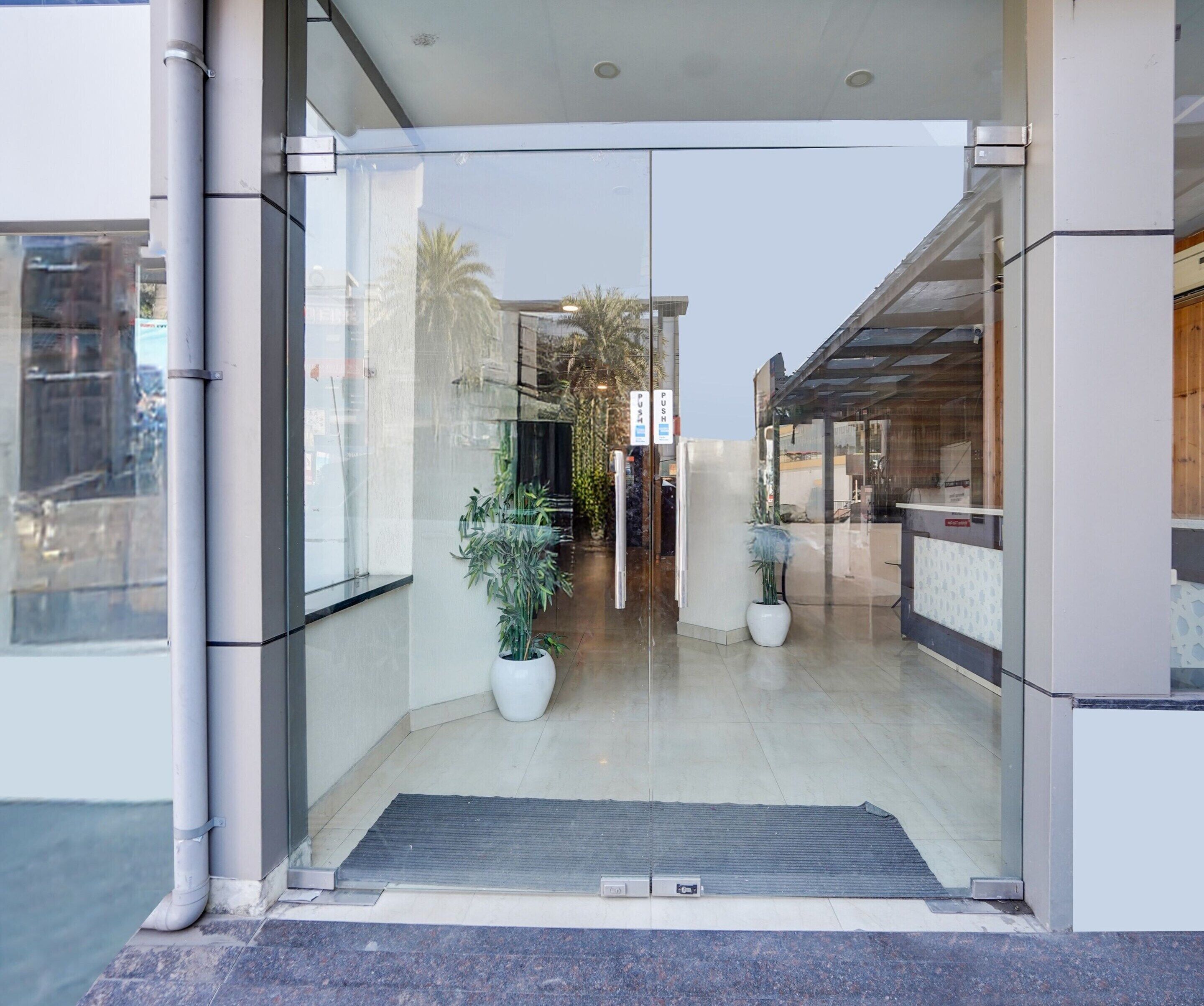 A modern building entrance with glass doors, a metal threshold, and potted plants.