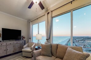 Ein Hotelzimmer mit großem Fenster, einem Flachbildfernseher, einer Couch, einer Lampe und einem Deckenventilator.