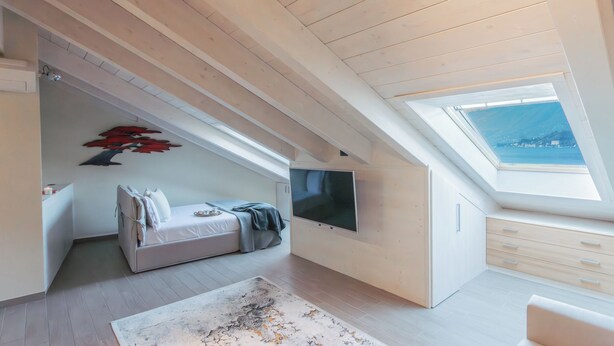 Een moderne loft slaapkamer met een schuine kap, een grote televisie, een bed, een bureau en uitzicht door een dakraam.