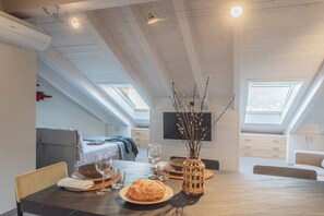 A dining area with a table set for two, a vase with branches, and a bed in the background. - Bellagio Prestige Loft by Rent All Como (Bellagio)