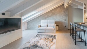 Een moderne loft met schuine plafonds, een witte bank, een keukenhoek en een grote televisie.