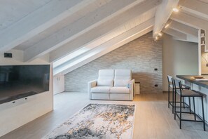 A modern loft with a sloped ceiling, a white sofa, a kitchen area, and a large TV. - Bellagio Prestige Loft by Rent All Como (Bellagio)
