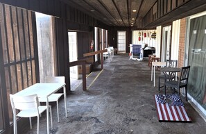 A covered outdoor seating area with tables and chairs, a fire extinguisher, and a flag on the ground. - BSI 101--Ocean-View Studio, Sleeps 2 Adults/2 Kids, Pool, Walk to Beach, Dogs OK (Port Aransas)