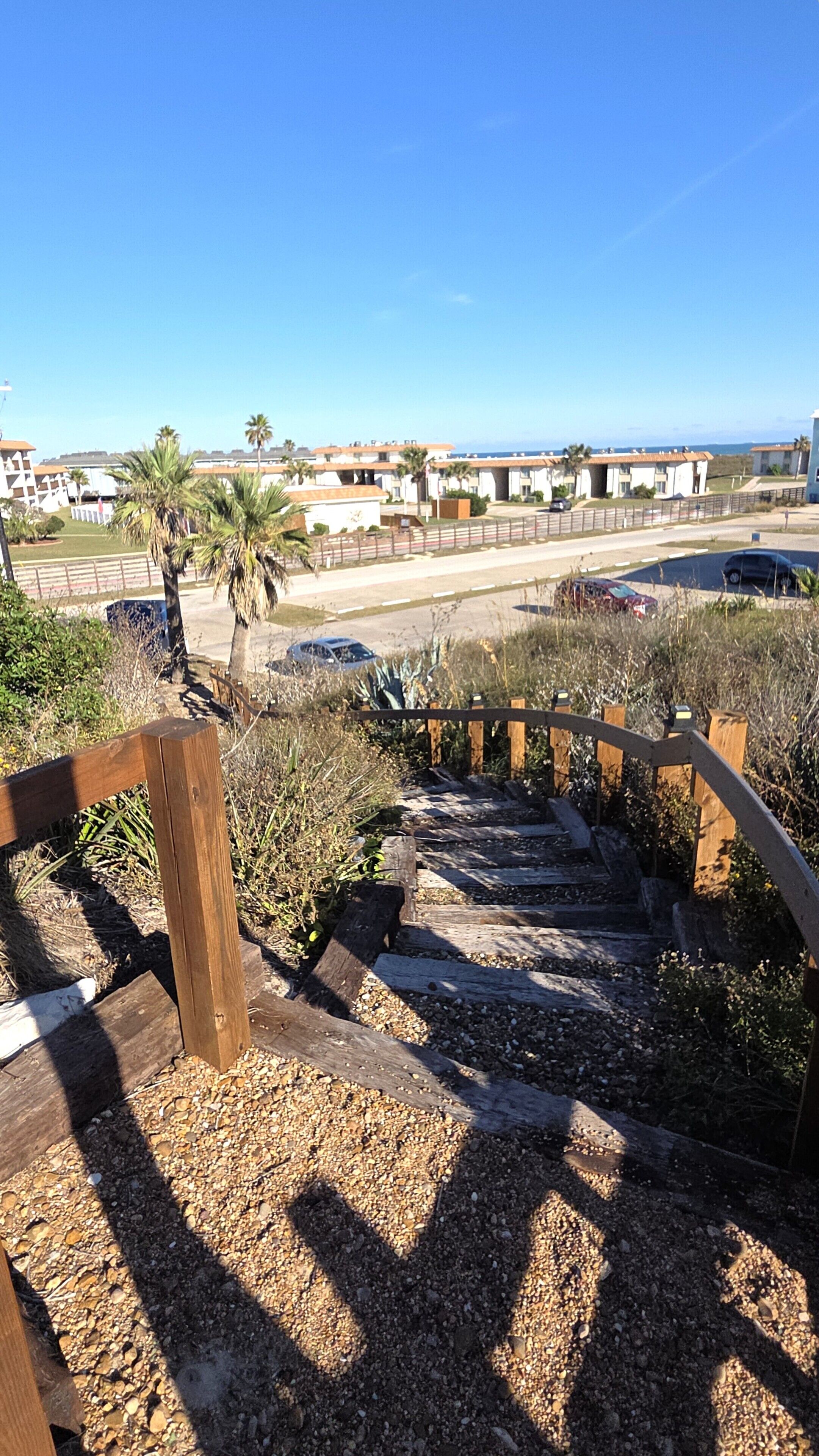 Un escalier en bois mène à une plage d’où l’on a une vue dégagée sur l’océan, avec une rangée de bâtiments blancs en arrière-plan.